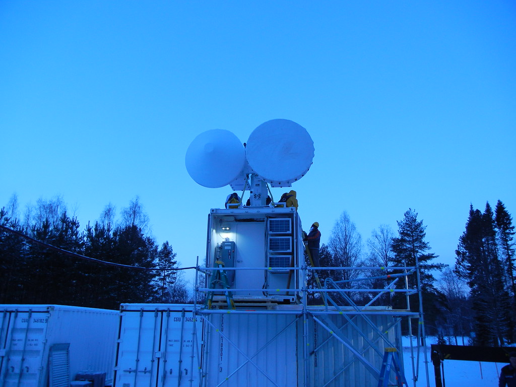 People stand on a container roof while installing radars in a forest clearing.